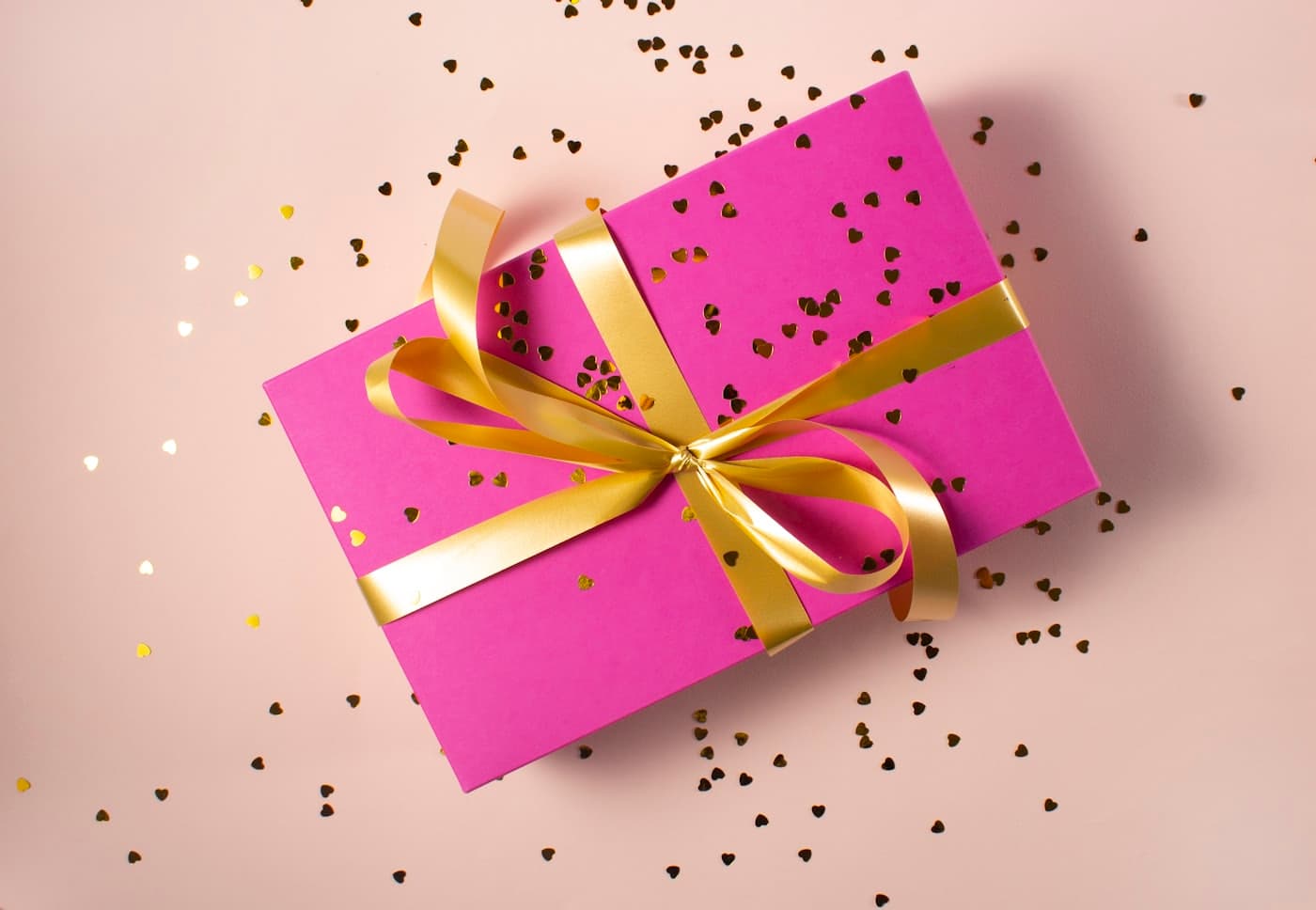 Bright pink gift box tied with a gold ribbon on a pastel background